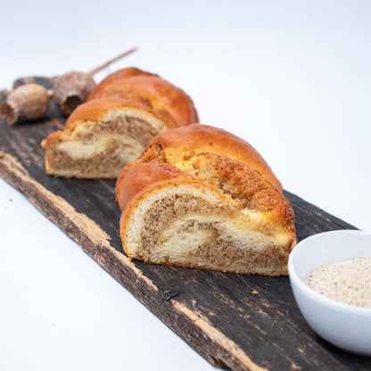 Zu sehen ist ein auseinandergeschnittener Weißmohnstriezel. Die zwei Hälften liegen nebeneinander und man sieht deutlich die saftige Weißmohnfülle. Im Hintergrund leicht verschwommen sieht man Weißmohnkapseln und im Vordergrund eine weiße Schale mit Weißmohnsamen. 